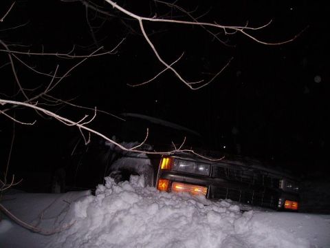 2000 Chevrolet Tahoe - A dark SUV is stuck in a large snowdrift at night, with its headlights illuminated.