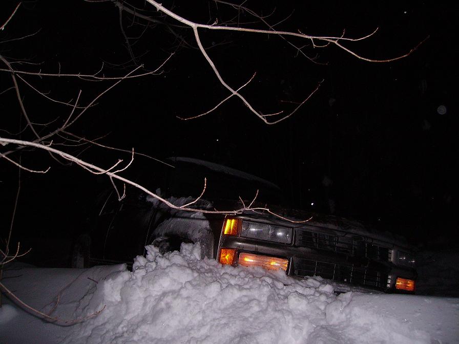 Front view of a dark SUV stuck deep in snow, headlights on