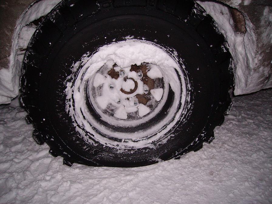 Tire and wheel covered in snow, showing lug nuts and a rusty rim