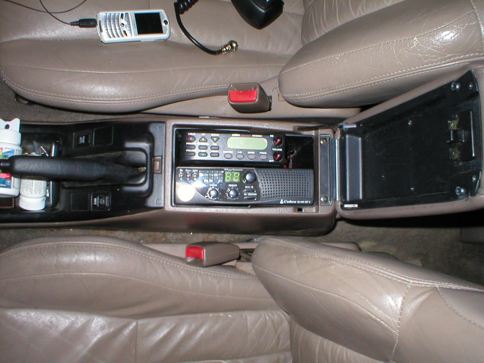 Tan leather car interior showing center console with CB radio, handheld radio, and emergency brake