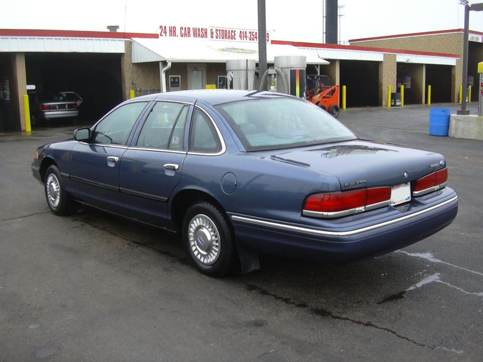 Blue sedan parked at a car wash. Another car is visible inside one of the wash bays