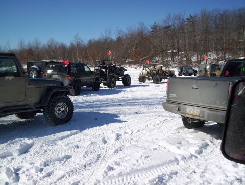 2002 Jeep Wrangler - A group of off-road vehicles are gathered in a snowy, wooded area under a clear blue sky.