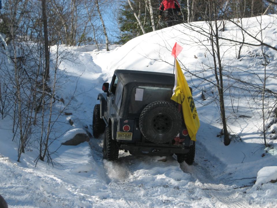 Rear view of a black 2002 Jeep Wrangler driving on a snowy trail with a yellow flag attached