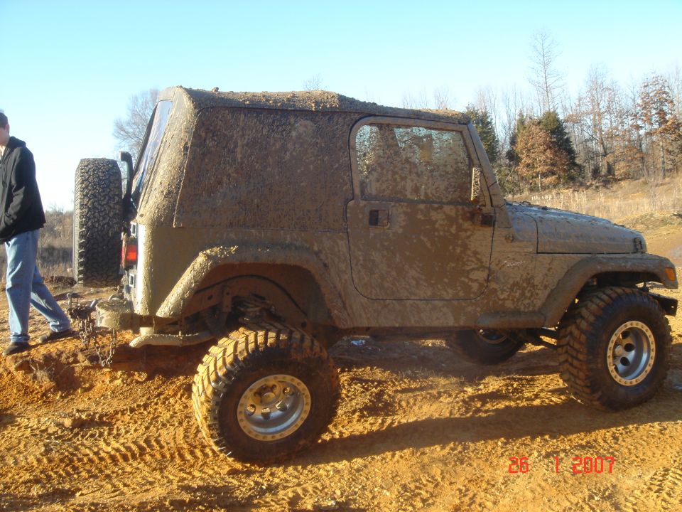Mud-covered Jeep Wrangler parked on a dirt road with a person standing nearby