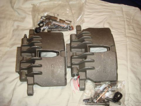 1993 Ford Taurus - Two brake calipers and a bag of hardware are laid out on a white, textured surface.