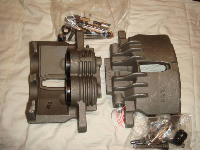 Two brake calipers and a bag of hardware on a white surface