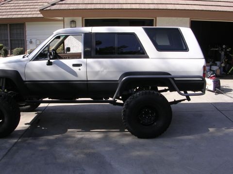 1985 Toyota 4Runner - Side view of a modified white Toyota SUV with off-road tires and protective bars.