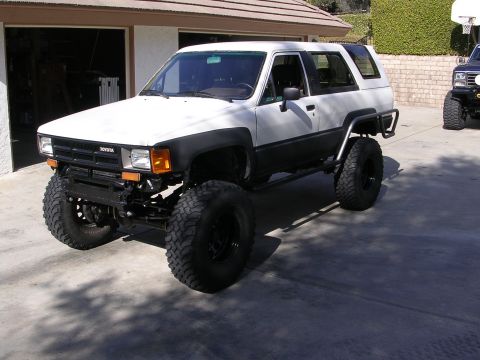 1985 Toyota 4Runner - A modified 1985 Toyota 4Runner is shown with aftermarket bumpers and suspension, parked outside a garage.