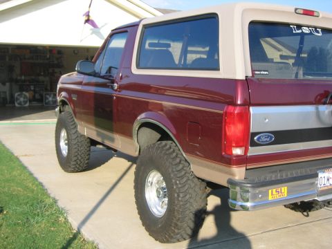 1996 Ford Bronco - Maroon Ford Bronco with tan trim and lifted suspension, viewed from the rear three-quarter angle.