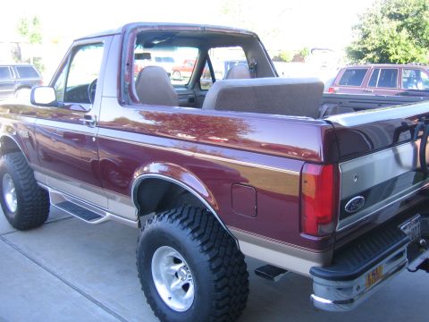 1996 Ford Bronco - Maroon 1996 Ford Bronco with tan trim and removable top, lifted with large tires.