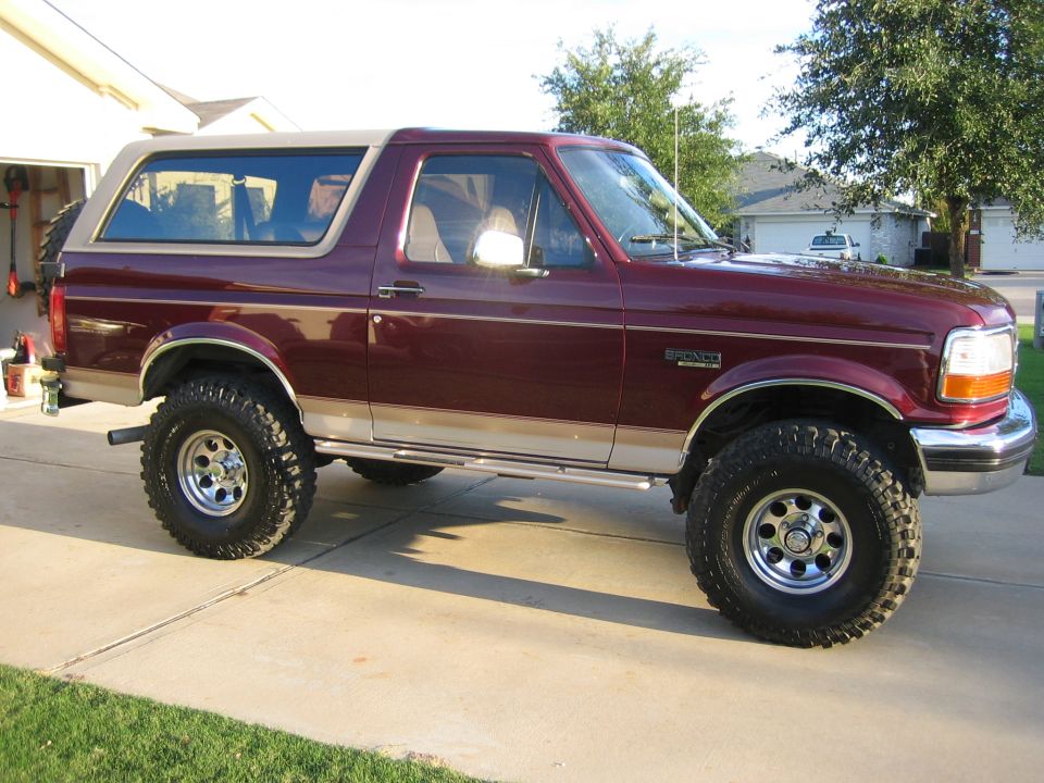 Burgundy and tan lifted Ford Bronco SUV parked in driveway, passenger side view