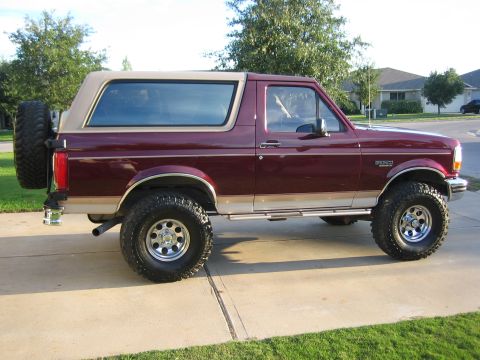 1996 Ford Bronco - Side view of a maroon 1996 Ford Bronco SUV with a tan removable top and a spare tire mounted on the back.