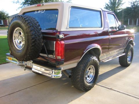 1996 Ford Bronco - Rear view of a maroon Ford Bronco with a spare tire and a tan removable top. The vehicle has a two-tone paint scheme.