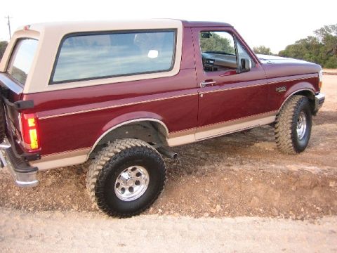 1996 Ford Bronco - Maroon 1996 Ford Bronco with tan top and off-road tires sits on a dirt surface.