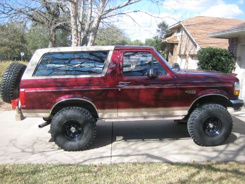 1996 Ford Bronco - Side view of a red 1996 Ford Bronco with a tan stripe and a spare tire on the back.