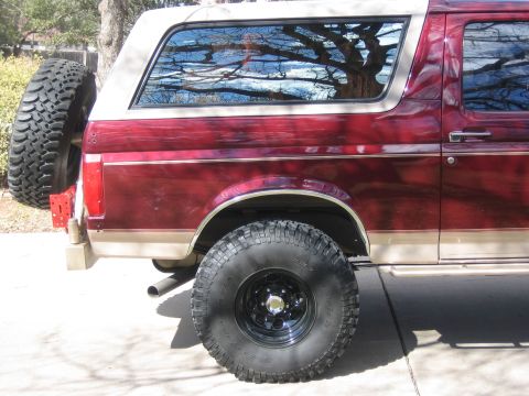 1996 Ford Bronco - Rear view of a red and tan 1996 Ford Bronco, showing the spare tire mounted externally.