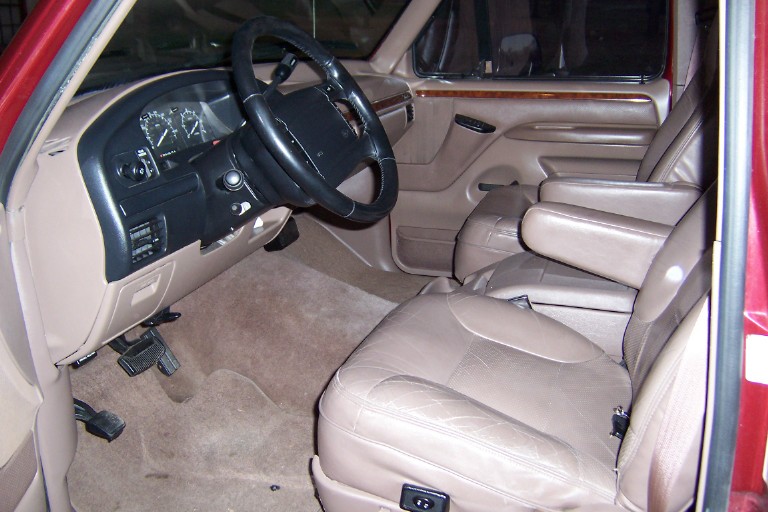 Tan leather interior of a Ford truck with black dash, leather steering wheel and woodgrain door trim
