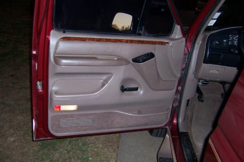 1996 Ford Bronco - Interior view of a red SUV's driver side door, showing tan door panel and part of the dashboard.