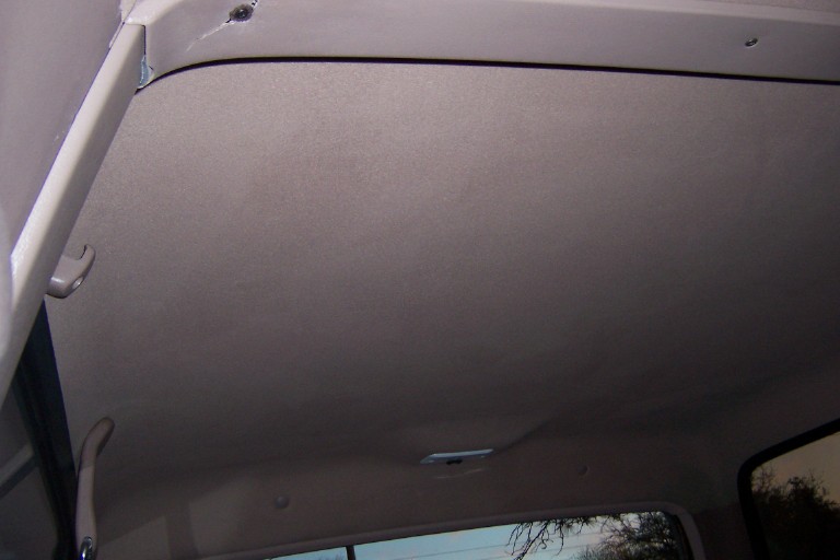 Tan cloth headliner with grab handle, coat hook and dome light inside truck cab