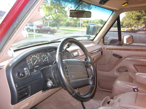 1996 Ford Bronco - The interior of a truck, a tan dashboard, steering wheel, and leather seats, with a view of the street through the windshield.