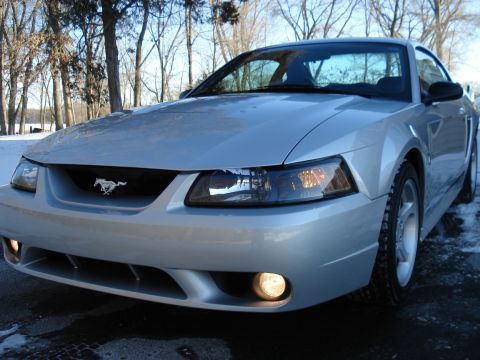 1998 Ford Taurus - A silver Ford Mustang is parked outside in the winter, showing its front grille and headlights.