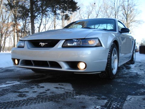 1998 Ford Taurus - A silver Ford Mustang is parked on a snowy road, its headlights and fog lights illuminated.