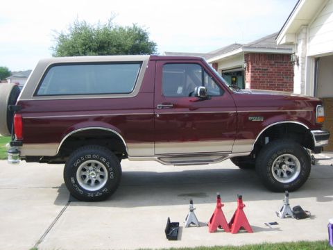 1996 Ford Bronco - Side view of a maroon 1996 Ford Bronco with a tan removable top and a spare tire mounted on the rear.