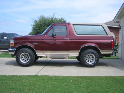 1996 Ford Bronco - Side profile of a maroon 1996 Ford Bronco with a tan removable top, parked in front of a house.
