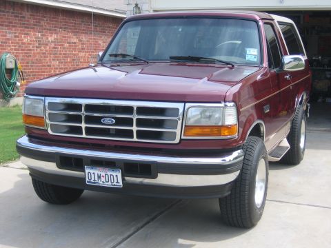 1996 Ford Bronco - This maroon Ford Bronco is shown from the front, parked in a driveway with a brick house in the background.