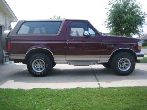 1996 Ford Bronco - A maroon and tan 1996 Ford Bronco SUV is shown from the side, parked on a concrete driveway.