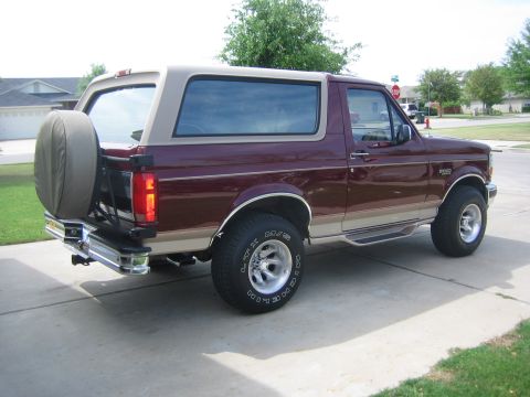 1996 Ford Bronco - Maroon and tan 1996 Ford Bronco shown from the rear quarter angle, a spare tire mounted on the rear.