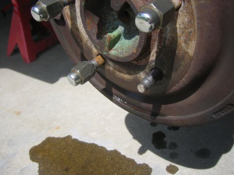 1996 Ford Bronco - A close-up view of a vehicle's rusty wheel hub and brake rotor, with a puddle of liquid on the ground.