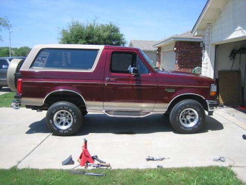 1996 Ford Bronco - A maroon 1996 Ford Bronco with a tan removable top is parked in a driveway next to a garage.