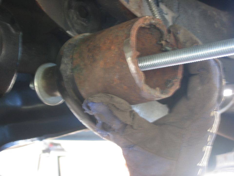 Gloved hand working on rusted metal pipe with threaded rod