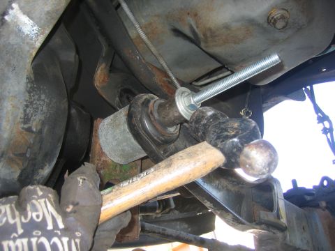1996 Ford Bronco - Close-up of a mechanic using a hammer and bolt to install a suspension bushing on a vehicle.