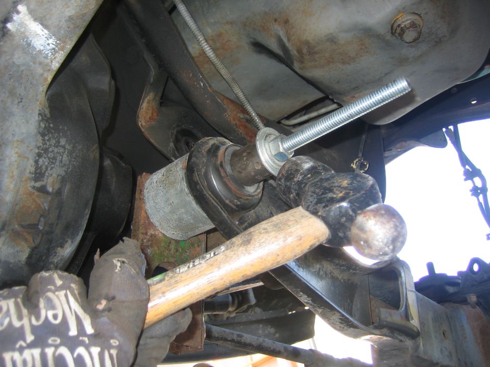 Hammer hitting a bolt on a vehicle's suspension bushing