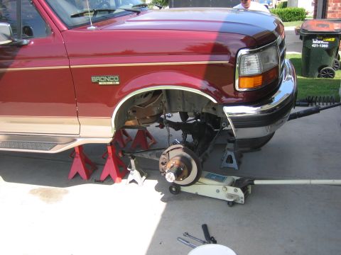 1996 Ford Bronco - A red Ford Bronco with tan trim is elevated on jack stands, undergoing suspension work.