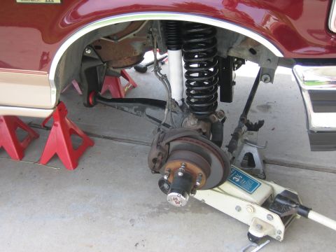1996 Ford Bronco - The suspension of a maroon Ford Bronco is visible, supported by jack stands and a hydraulic jack.