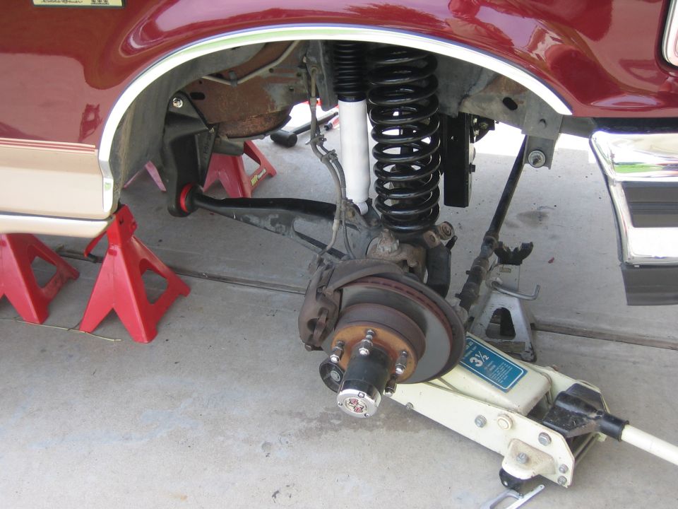 Maroon Ford Bronco front suspension on jack stands, showing lifted coilover and brake assembly