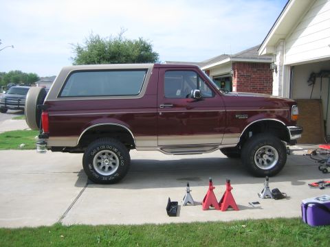 1996 Ford Bronco - A lifted Ford Bronco is parked in a driveway with jack stands nearby, suggesting recent maintenance or modification.