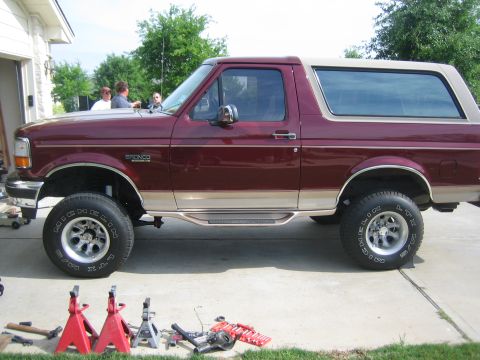 1996 Ford Bronco - A maroon 1996 Ford Bronco with a tan top is parked on jack stands, suggesting a lift installation is in progress.