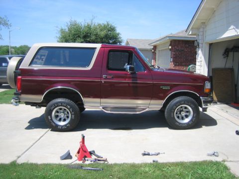1996 Ford Bronco - A maroon 1996 Ford Bronco with a tan removable top is parked in a driveway with tools and a jack nearby.