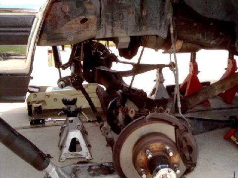 1996 Ford Bronco - The vehicle's undercarriage is visible, supported by jack stands, with suspension and brake parts exposed.