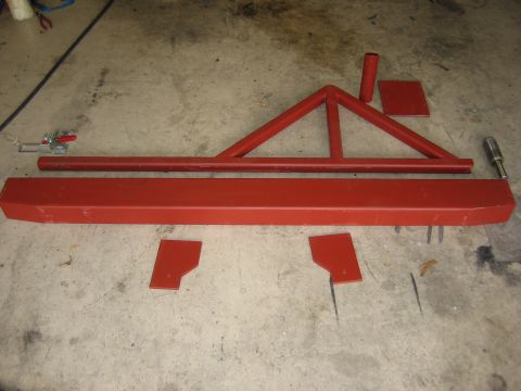 1996 Ford Bronco - Fabricated steel rear bumper components laid out on a shop floor in red oxide primer: a boxed bumper shell, a triangulated tube tire-carrie…