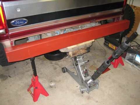1996 Ford Bronco - A red metal bar is being installed under the rear of a Ford truck, which is supported by jack stands and a floor jack.
