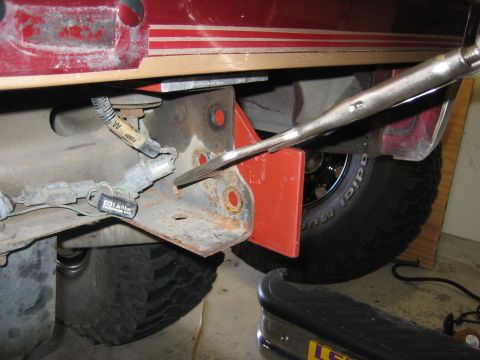 1996 Ford Bronco - A tool is used to work on a rusted bracket attached to the vehicle's frame near the rear tire.