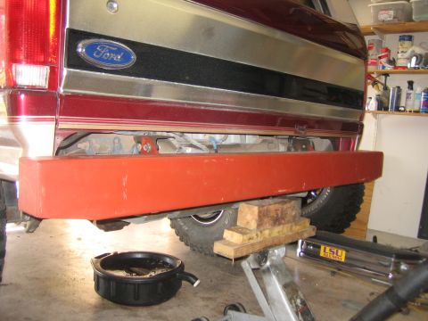 1996 Ford Bronco - The rear of a red Ford Bronco is shown with a new red bumper being installed, with a drain pan underneath.