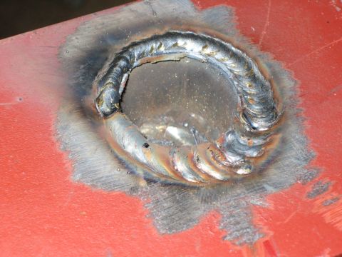 1996 Ford Bronco - Close-up view of a circular opening reinforced with welding on a red painted metal surface.