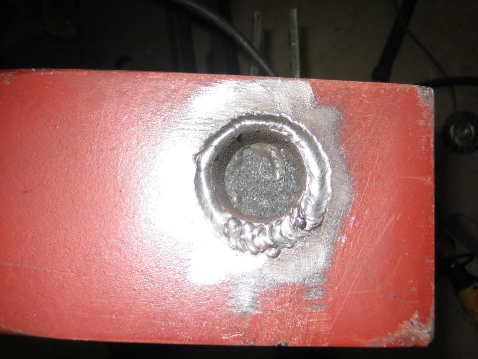 Red metal bar with a circular weld and metal shavings inside the hole