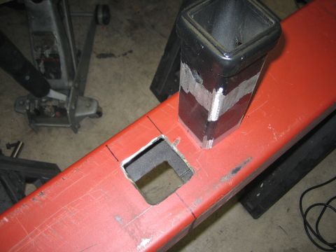 1996 Ford Bronco - A red metal beam is being modified with a square cutout and a black tube welded on top.